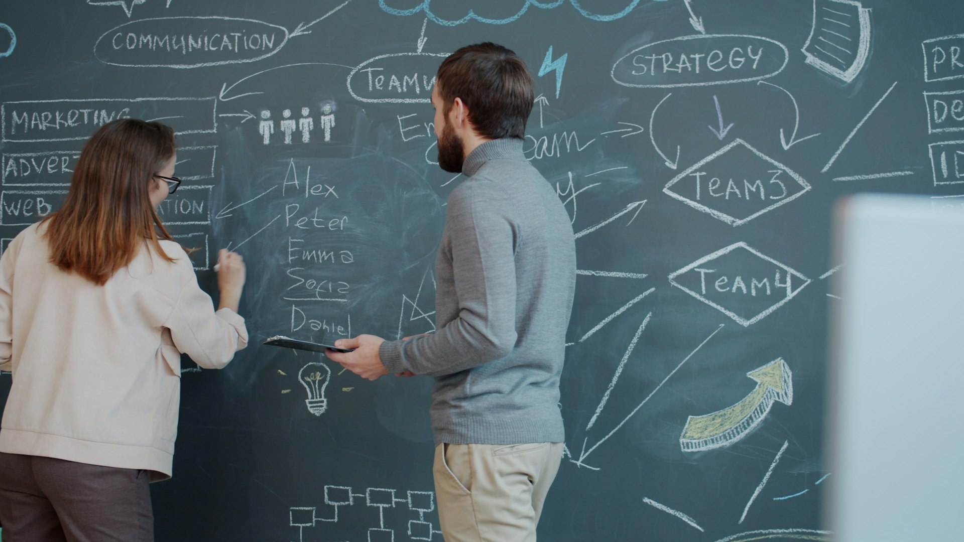 Two people planning on a chalkboard with diagrams.
